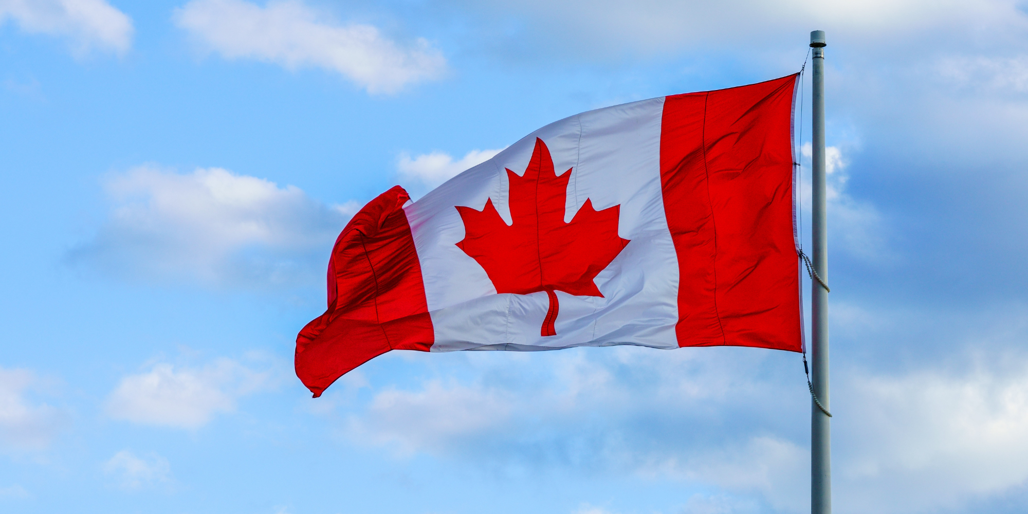 A picture of the Canadian flag against a blue sky with clouds.