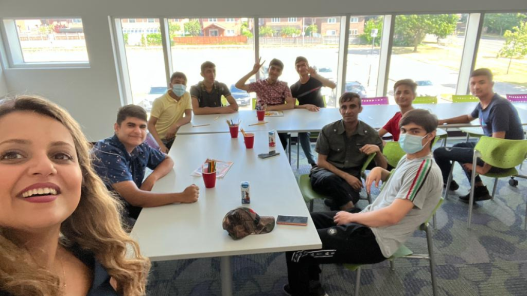 Group of young people sitting at a table. In the foreground is the facilitator who is also taking the pictures.