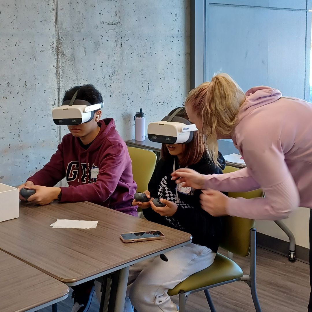 Two young people testing Virtual Reality Headsets. An instructor is helping them.