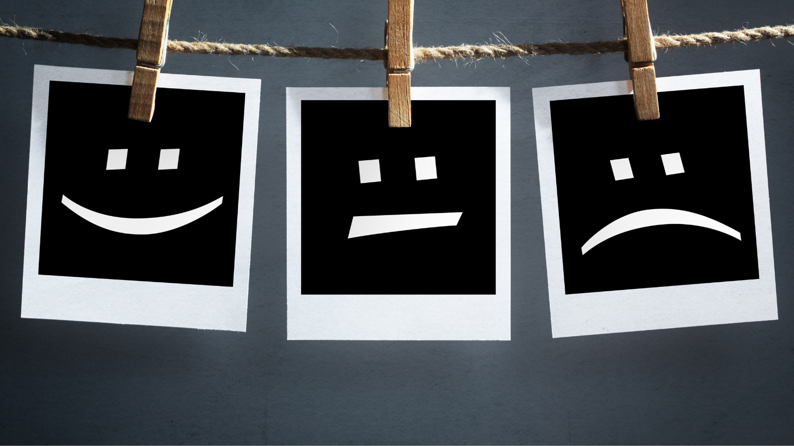 Three Polaroid pictures hang on a rope line with clothes pins. They show three graphic design faces (simple in style like a smiley face). One smiles, one has a straight mouth, and one is sad.