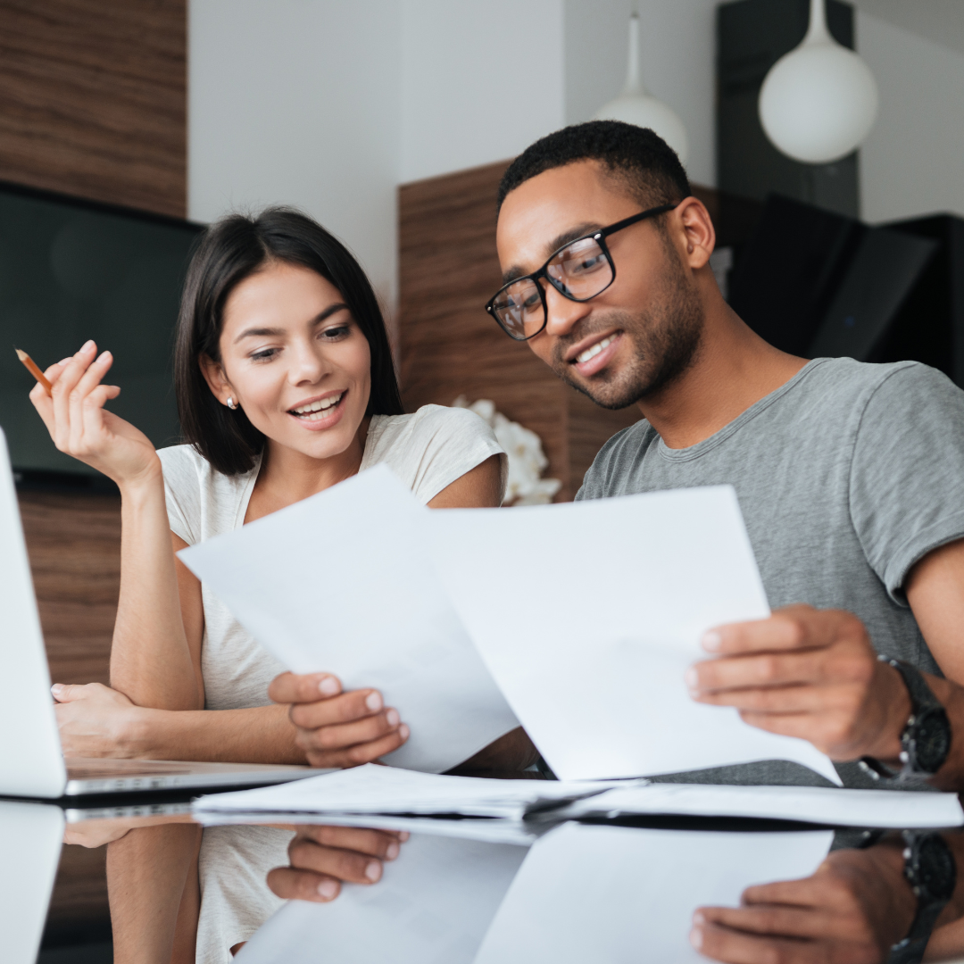Two young adults review paperwork together at a table, focused and engaged in discussion.