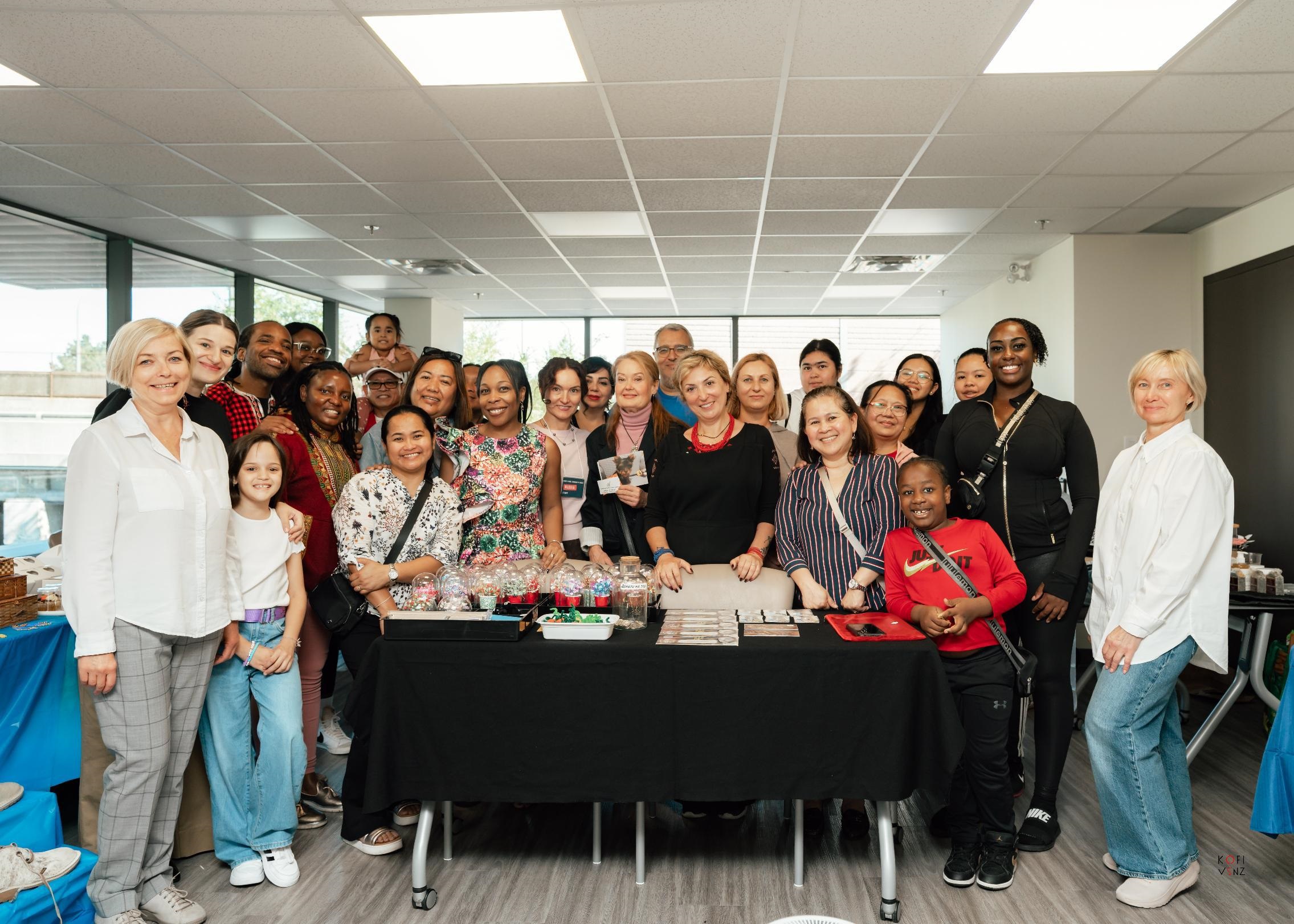 A group picture from the Business Networking Expo. A diverse group of individuals posed and smiling, gathered around a table filled with various products and trinkets.