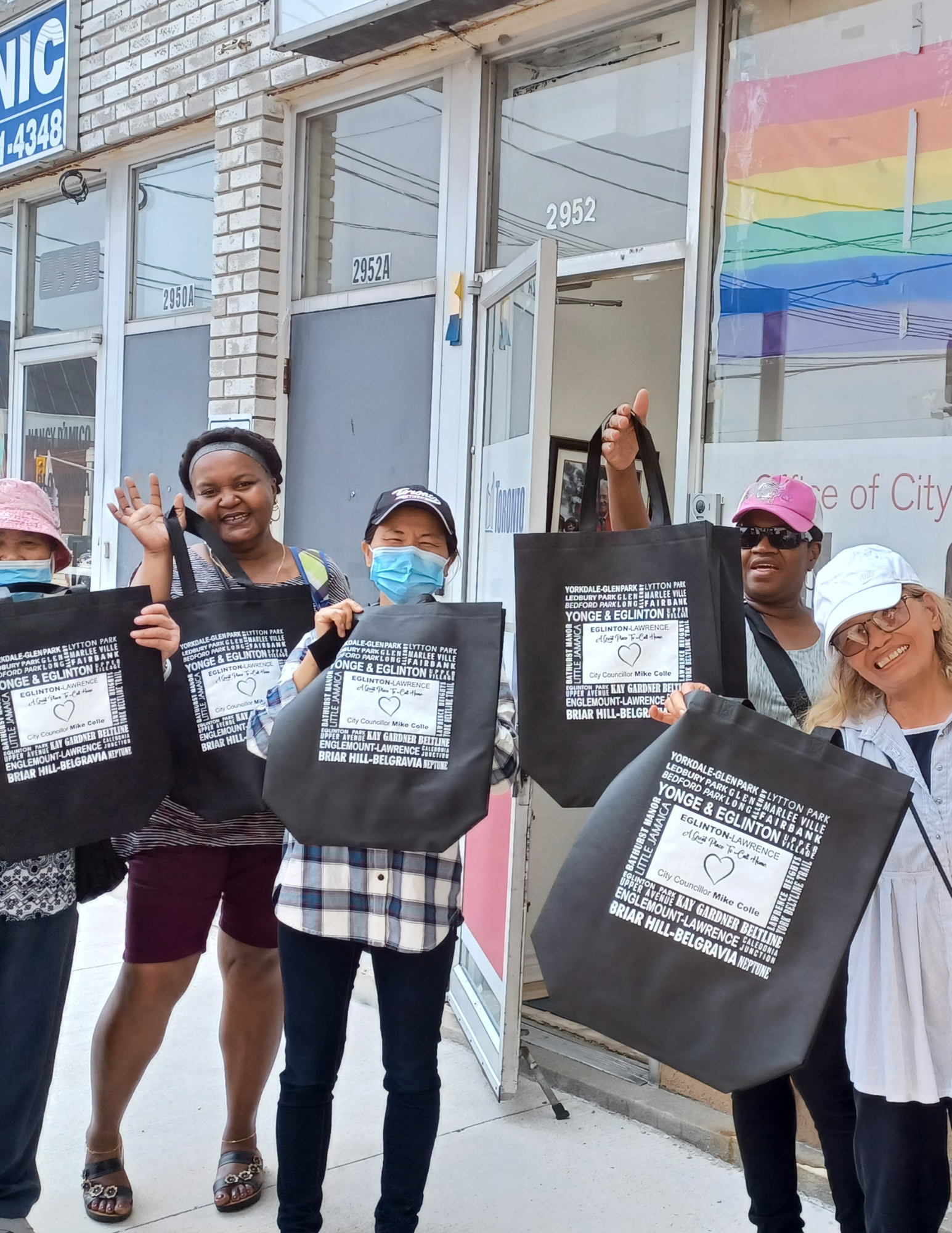 A group of people holding up tote bags in front of an office.