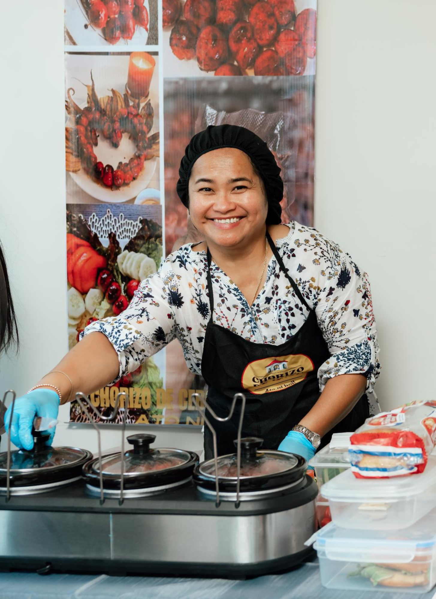 A person in an apron standing next to a table full of food.