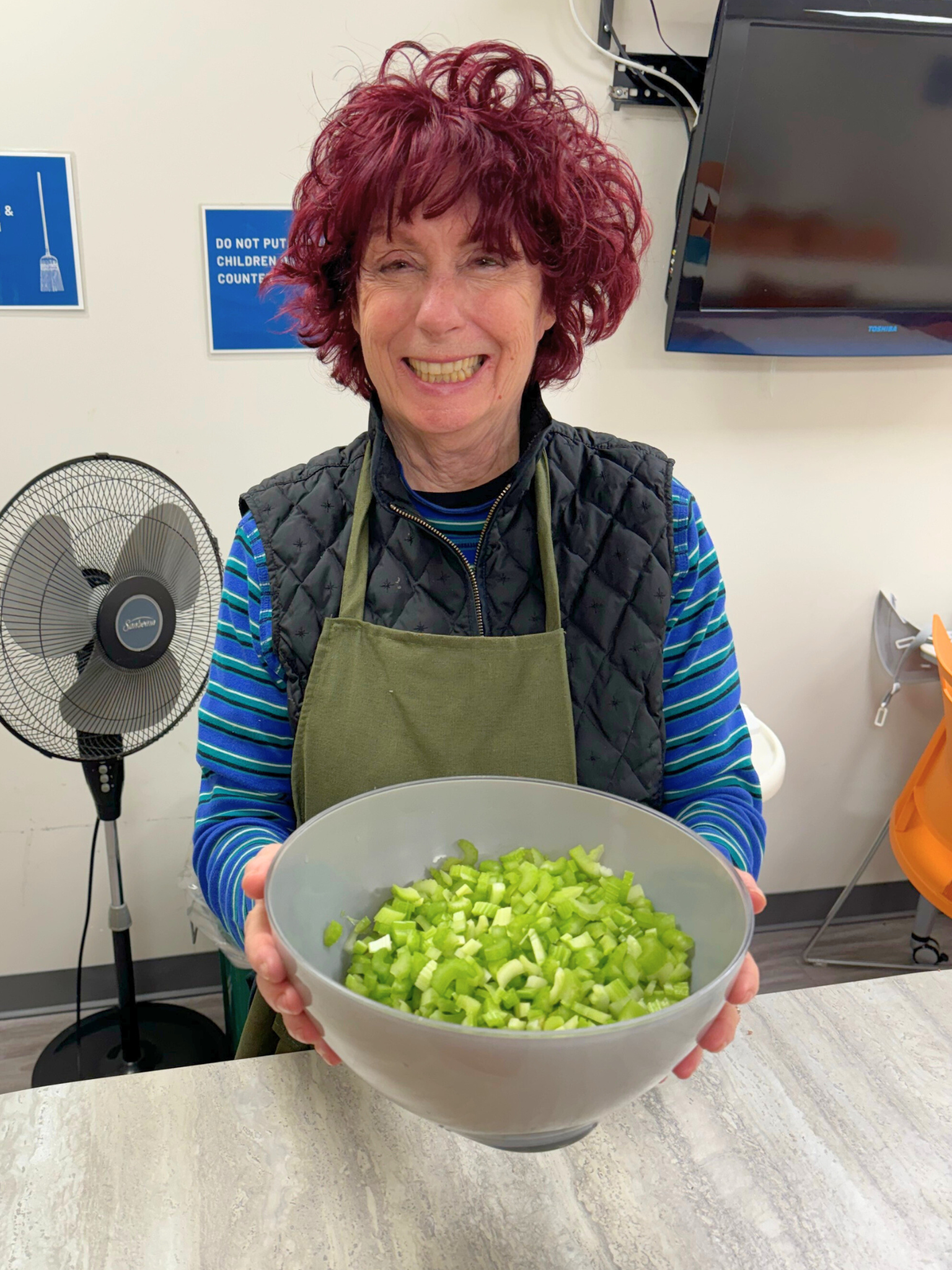 A woman holding a bowl full of diced celery and smiling.