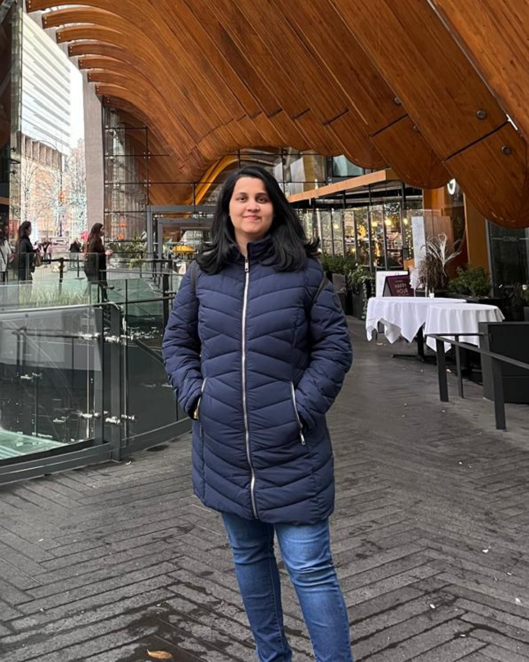 A picture of Archi standing in front of a modern building with arched wooden beams and glass facade.
