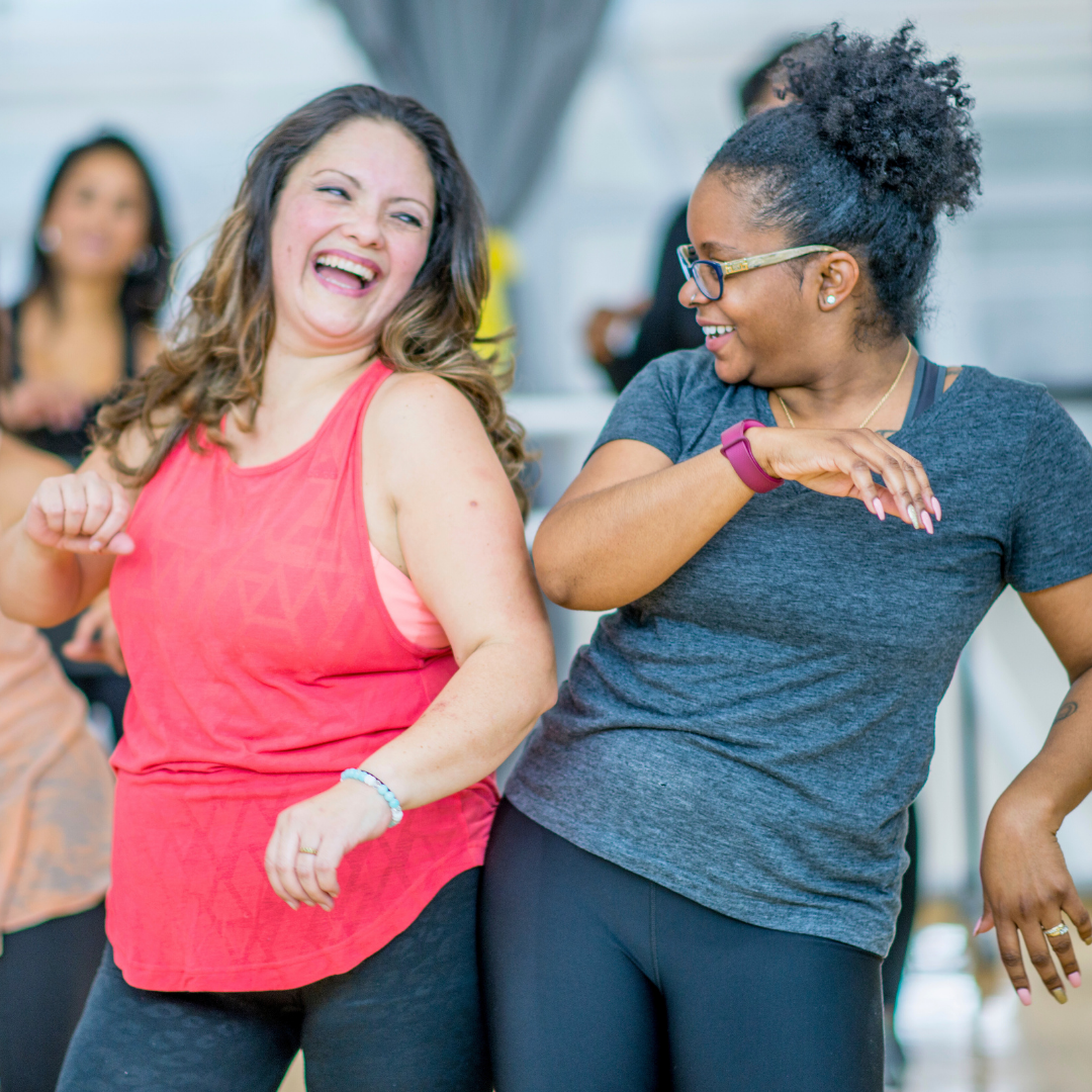 Two people smiling and dancing in a fitness class.
