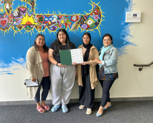Adriana and Farwa with their managers, Mandana and Elizabeth, standing in front of a colorful mural holding a certificate.