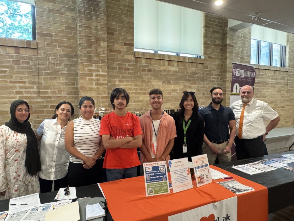 A group of eight people, including Farwa, standing behind a table with promotional materials.