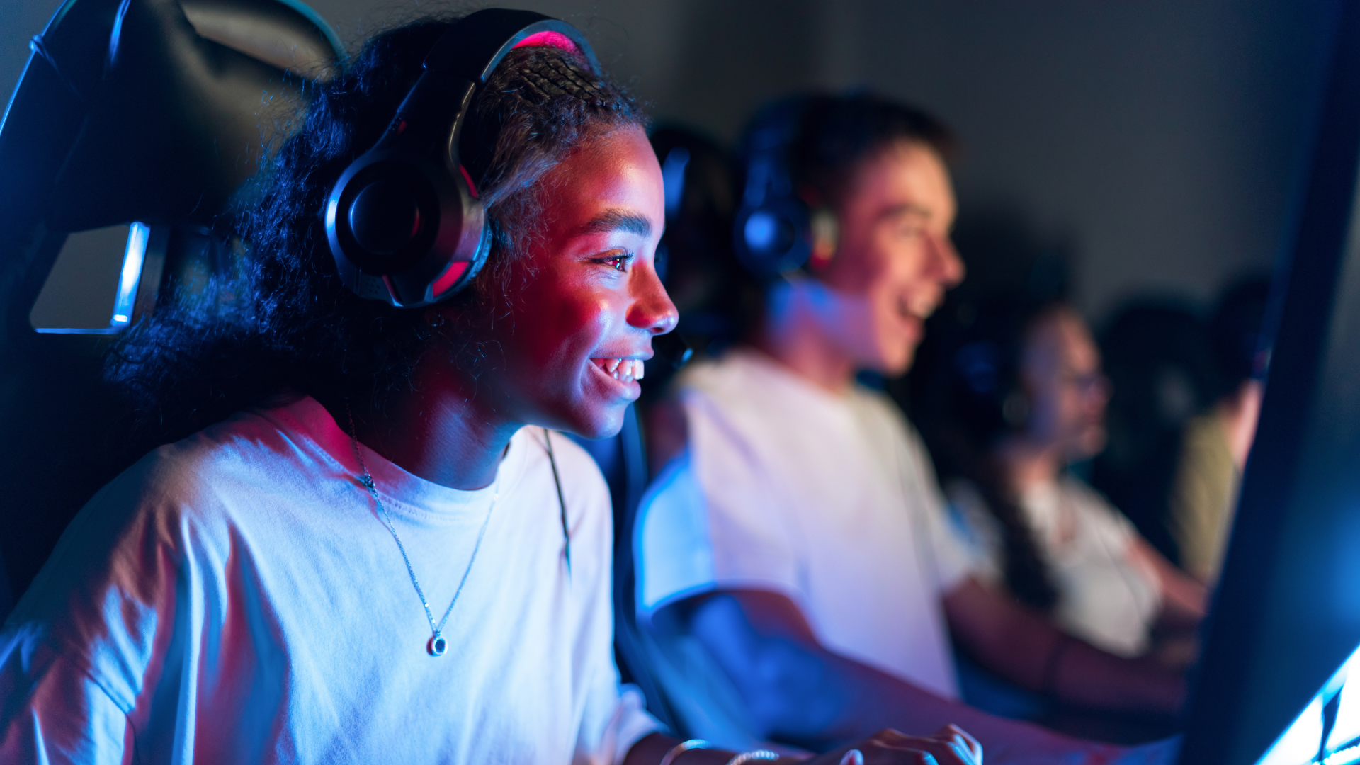 Three youth wearing headsets focused on computer screens in a dimly lit room.