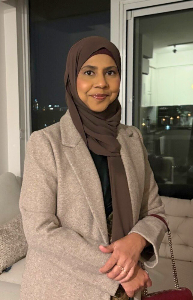 A picture of Aliya in a brown blazer smiling.