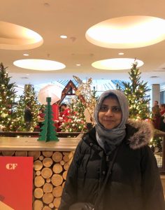 A picture of Aliya standing in a store in front of Christmas trees.