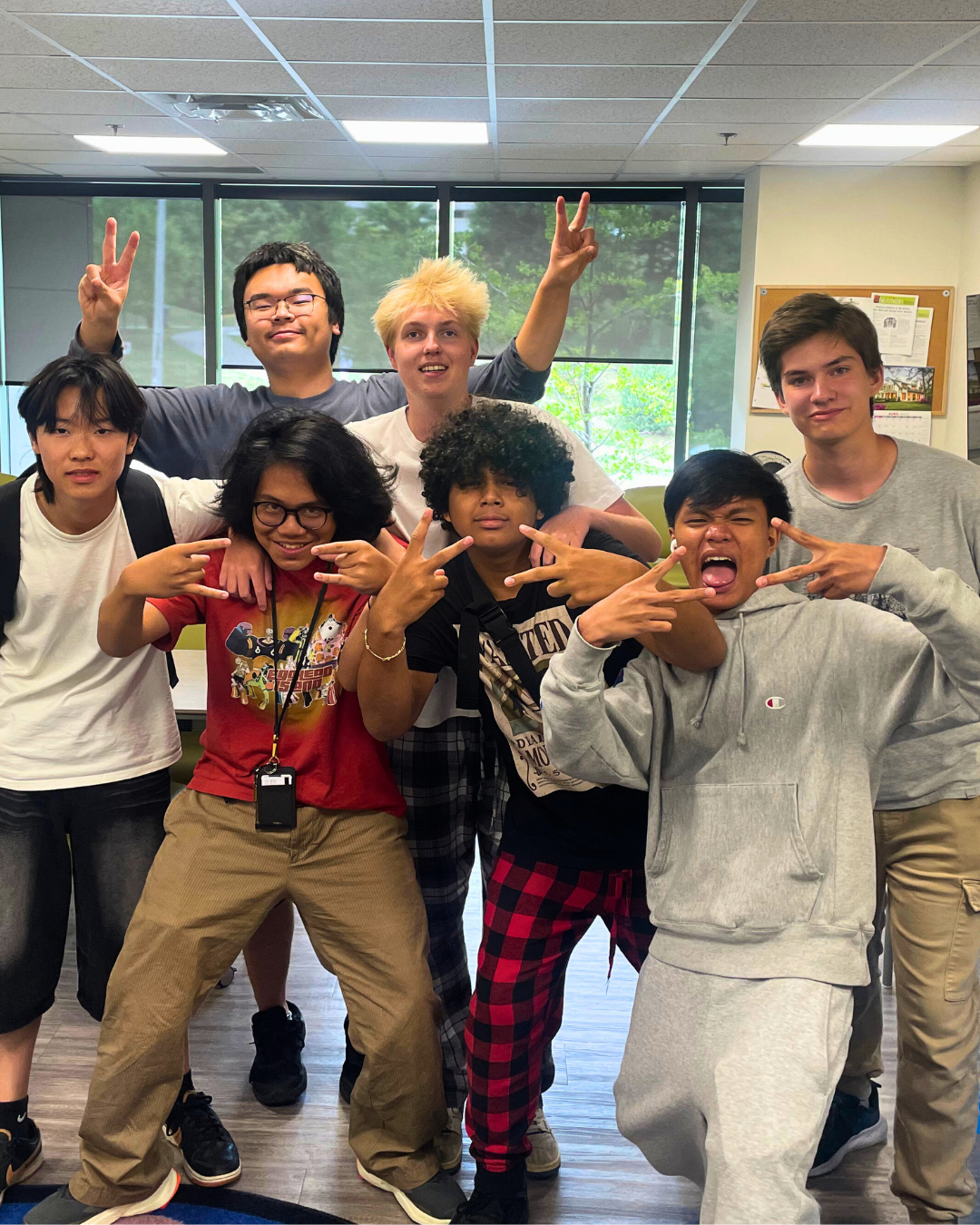 A group of youth posing indoors with playful expressions and hand gestures.