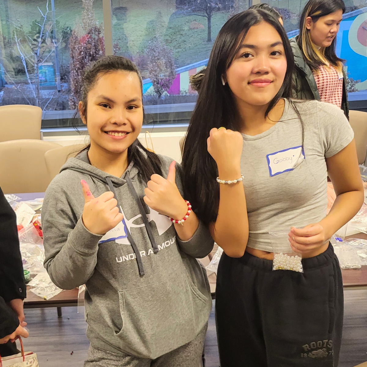 Two young women smiling in an indoor event, showing bracelets.