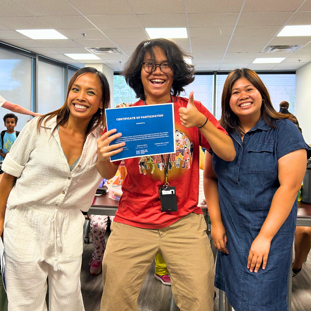 3 people standing smiling, one youth in the center holding up a certificate with a thumbs up.