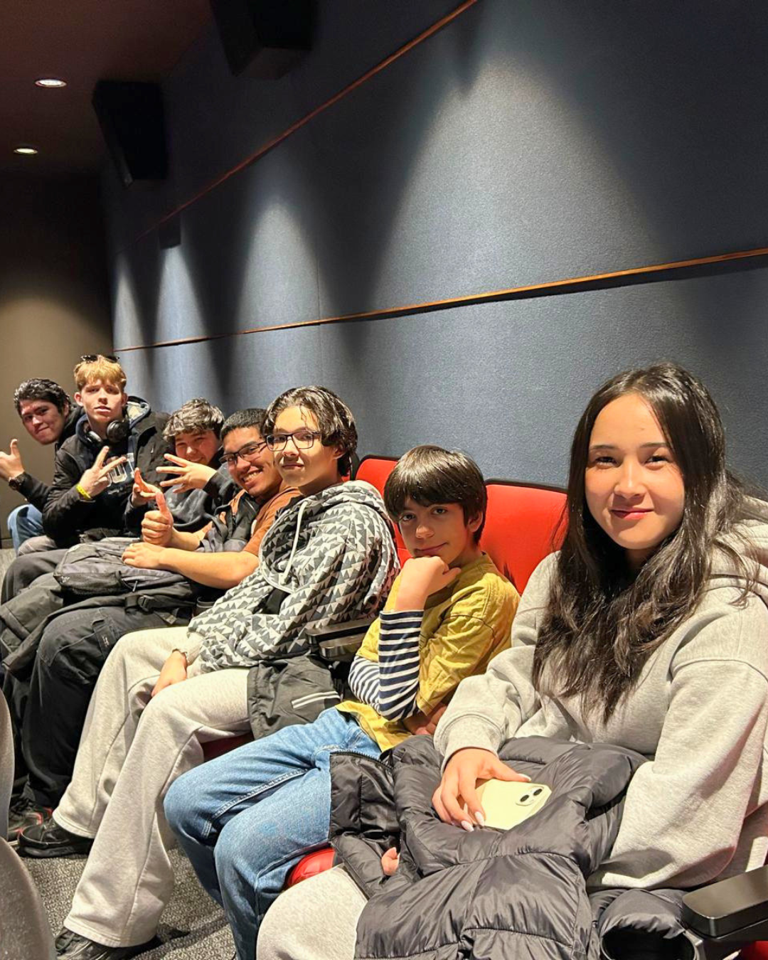 A group of youth sitting in a row of red seats in a movie theater.