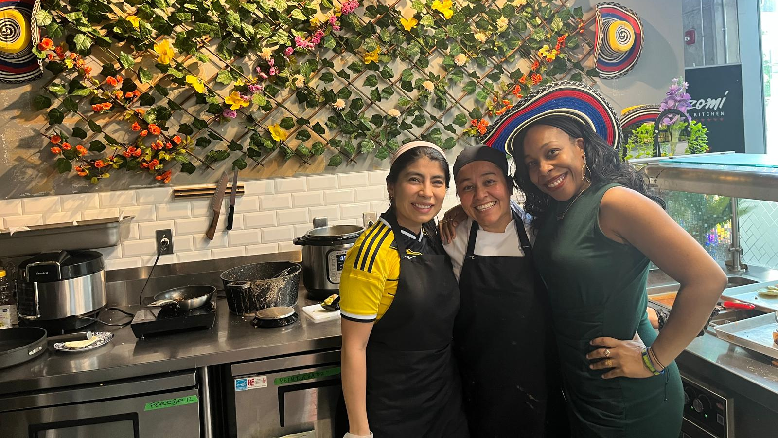 Three women stand smile at the cameral. They are standing in the food stall at the food court.
